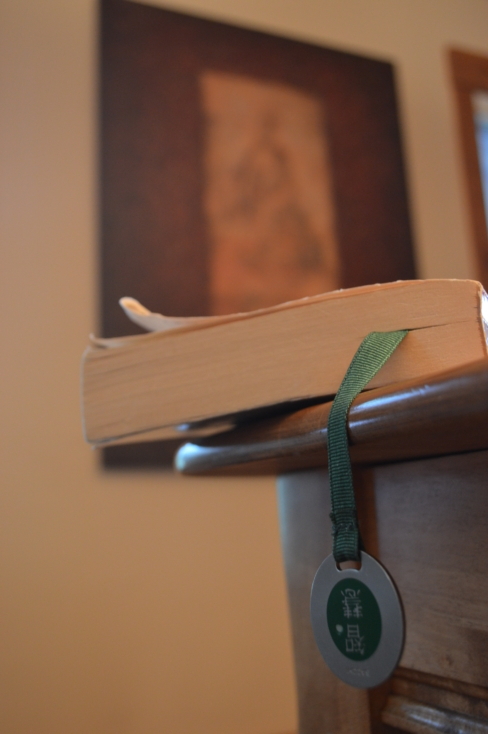 A book dangling off the edge of a table, closed with a page marked. There